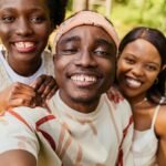 Three friends smiling for a selfie in a green park setting, exuding joy and friendship.